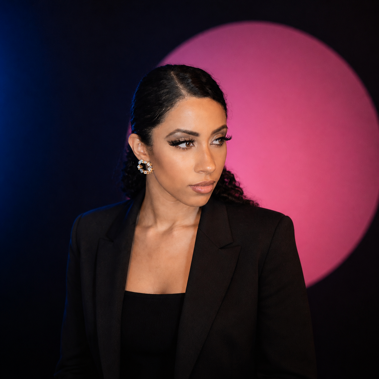 FAAN in a black blazer against a dark studio and pink circular light